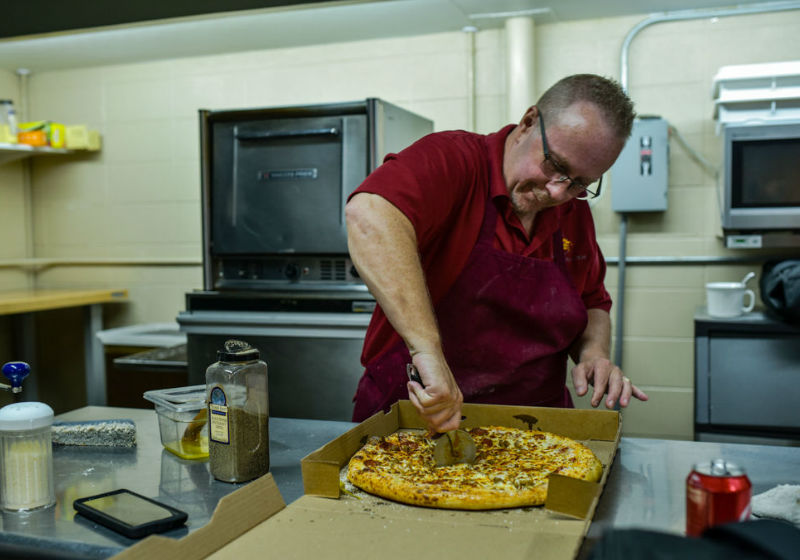 Jeff Minton corta um pedaço de pizza enquanto trabalha na 8th Street Pizza Foto: Tyler Stewart