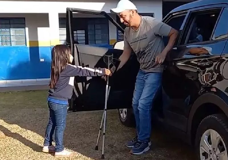 A menina Mariane Thielly, de 5 anos, ajudando o professor de matemática André Azevedo Paes de Barros, de 37 anos, que usa muleta, a descer do carro - Foto: reprodução / Campo Grande News