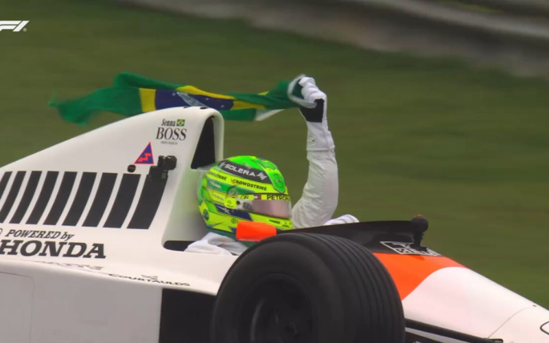 Com sua simpatia, Lewis Hamilton a exemplo do ídolo e homenageado, Ayrton Senna, levanta a Bandeira do Brasil pilotando a McLaren do nosso campeão eterno. - Foto: BandSport