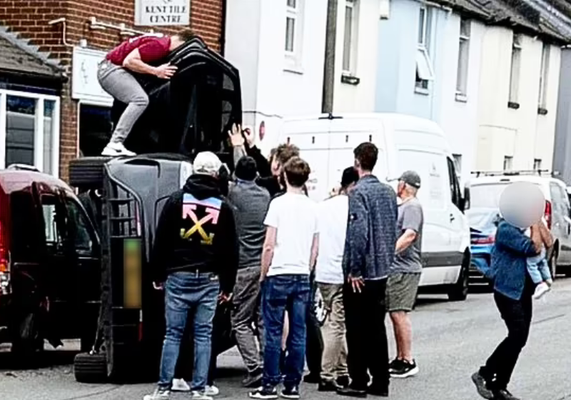 Os jovens salvando a família que capotou com o carro no Reino Unido. Um deles sai com o bebê no colo (dir). - Foto: SWNS. - Foto: Robert Winstanley/SWNS