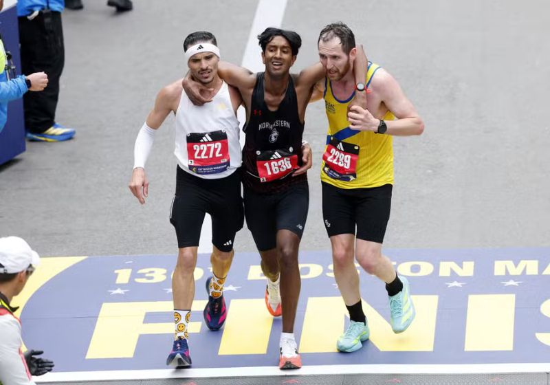 O brasileiro Robson de Oliveira (à dir) e o britânico Aaron Beggs (de amarelo) ajudam o corredor Ajay Haridasse, dos EUA a terminar a Maratona de Boston (EUA).- Foto: Reuters/Cj Gunther